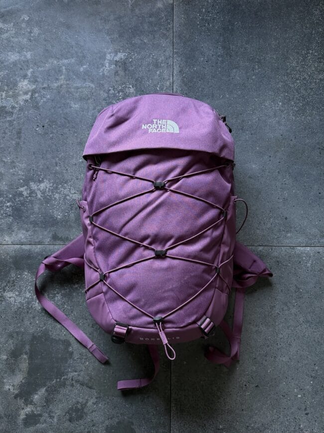 Purple The North Face backpack with crisscross bungee cords on a gray concrete floor