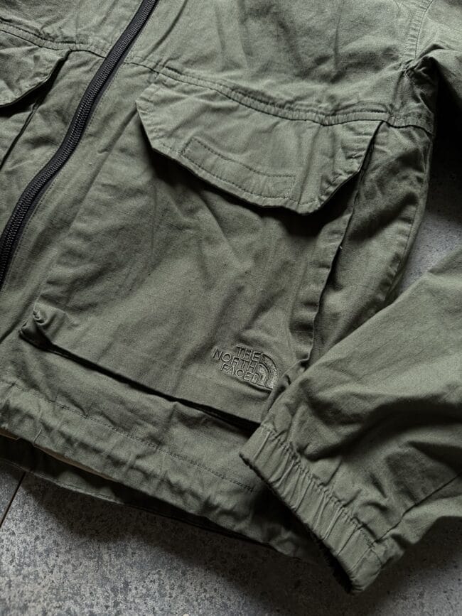 Olive-green North Face jacket with a zipper and front flap pocket, close-up detail.