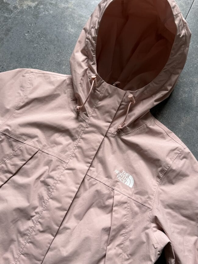 Light pink The North Face hooded jacket laid flat on a gray textured surface.