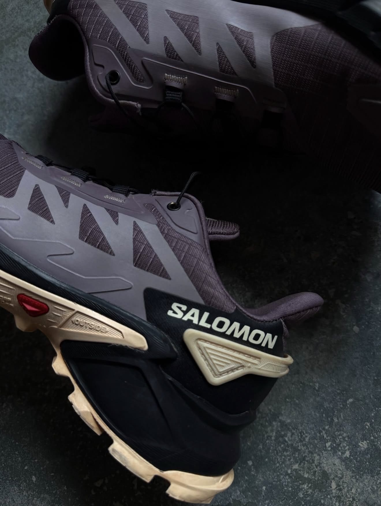 Close-up of a purple-gray Salomon hiking boot showing side panels, lugs, and beige sole detail for rugged outdoor use.