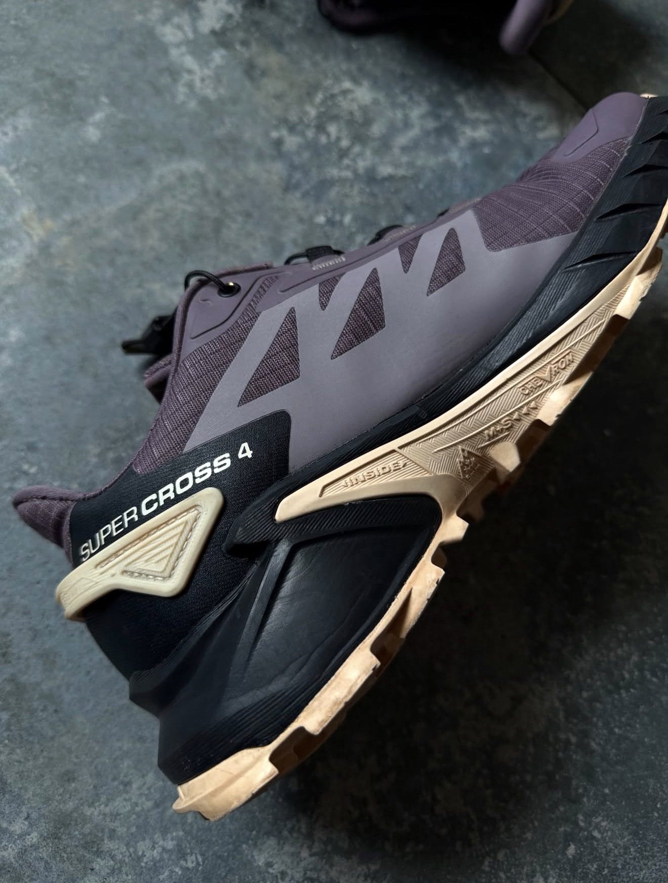 Close-up of a dark purple trail shoe with a tan rugged outsole and the label 'SUPER CROSS 4' on the side.