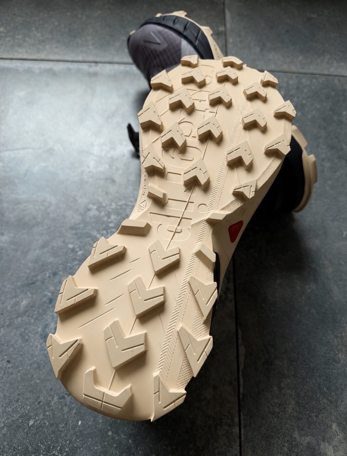 Beige outsole of a hiking boot with large rectangular lugs on a dark floor surface