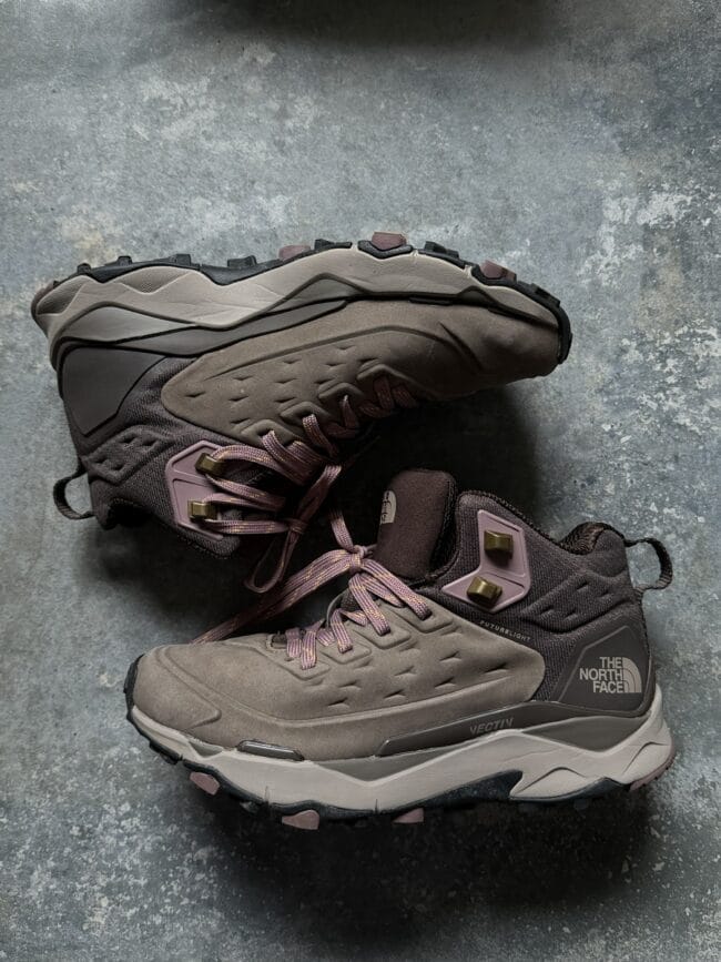 Pair of brown hiking shoes with rugged soles lying on a gray concrete floor; brand logo visible on the side (The North Face).