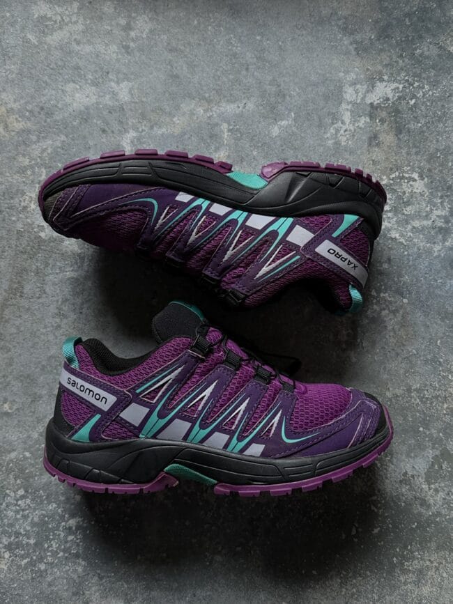 Pair of purple Salomon hiking shoes with teal accents resting on a gray textured surface