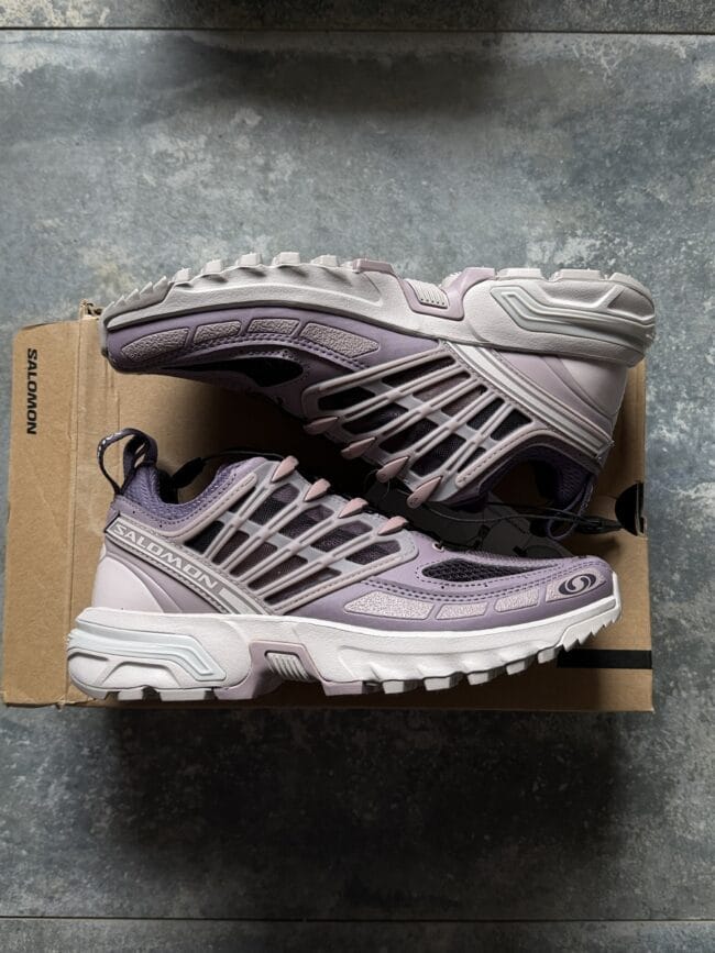 Lavender Salomon trail running shoe resting on a cardboard box, shown in side profile with a rugged lug sole.