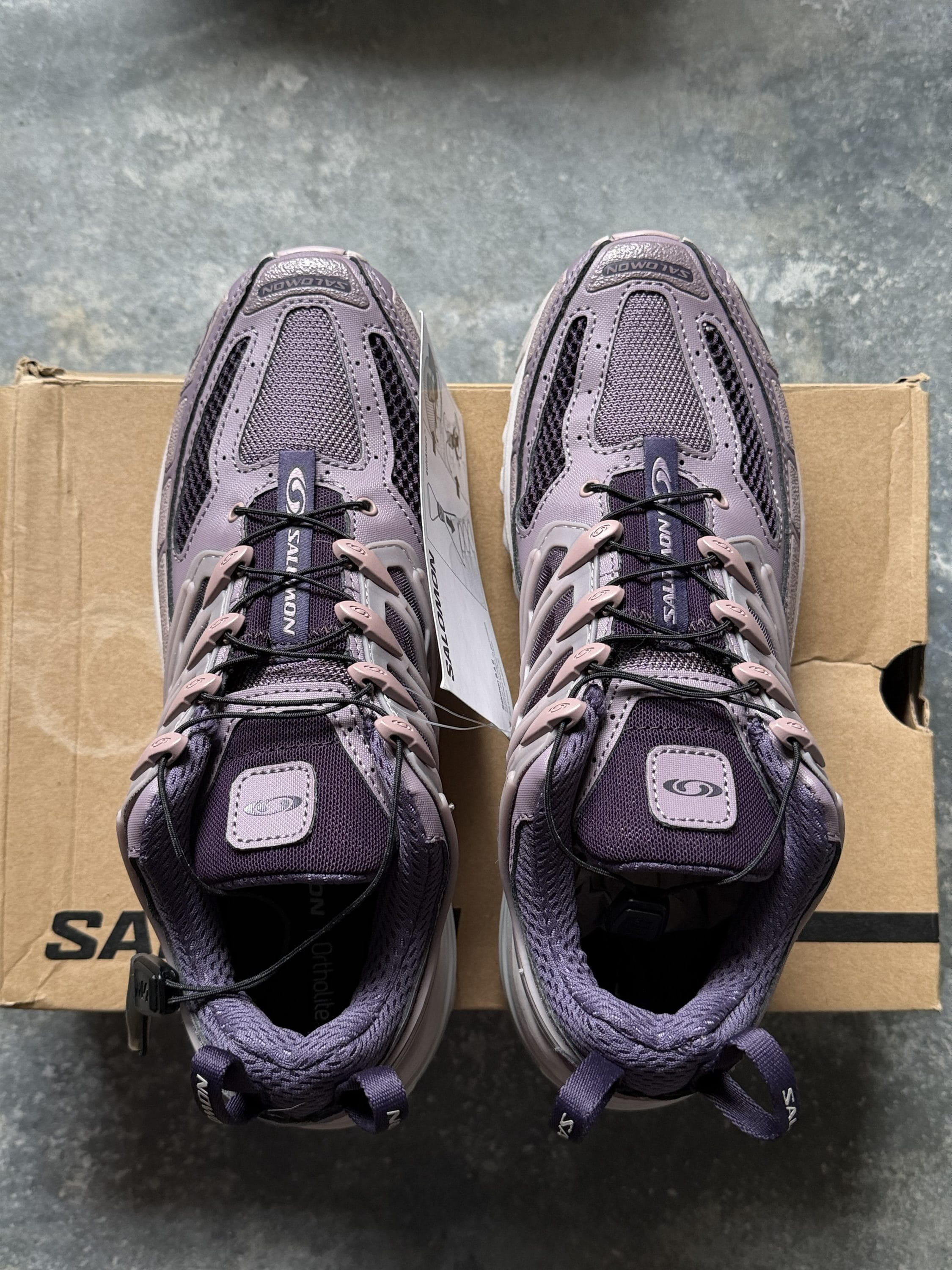 Top-down view of two purple Salomon hiking shoes resting on a cardboard box.