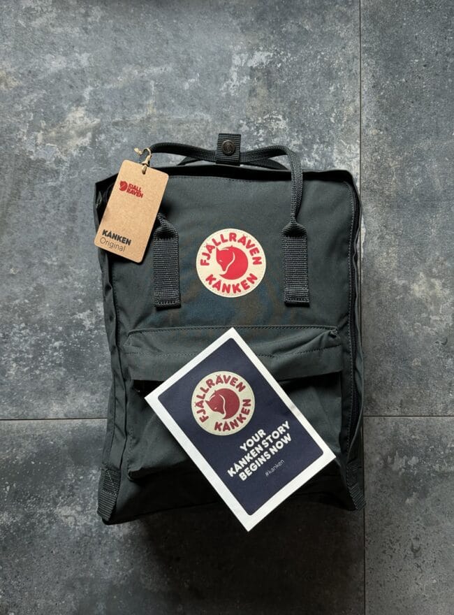 Black Fjallraven Kanken backpack with tag and logo on a dark textured floor