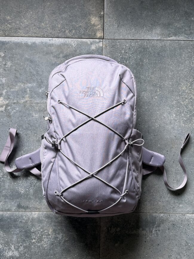 Purple North Face backpack placed on gray stone floor with crisscross bungee cords across the front.