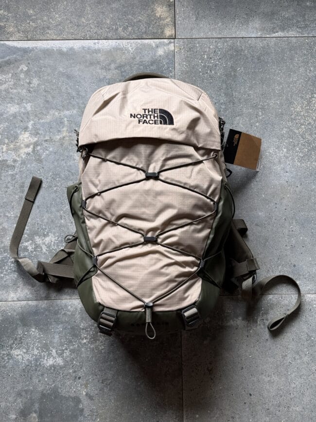 Beige The North Face hiking backpack with bungee cords laid on a grey tiled floor