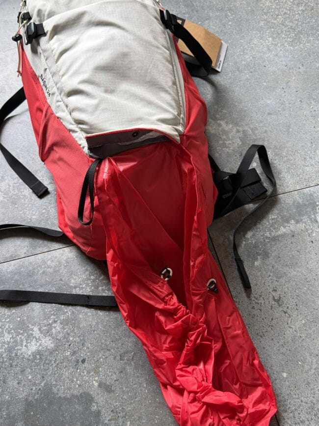 Red and light-gray backpack with black straps lying on a concrete floor