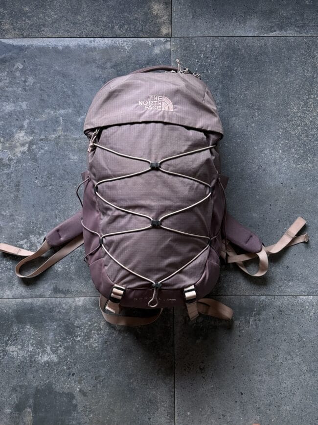 Brown The North Face backpack laid flat on a dark stone tiled surface with bungee cords across the front panel.