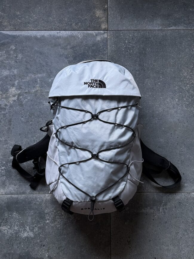 Top-down view of a light gray The North Face backpack with bungee cords on a stone floor.