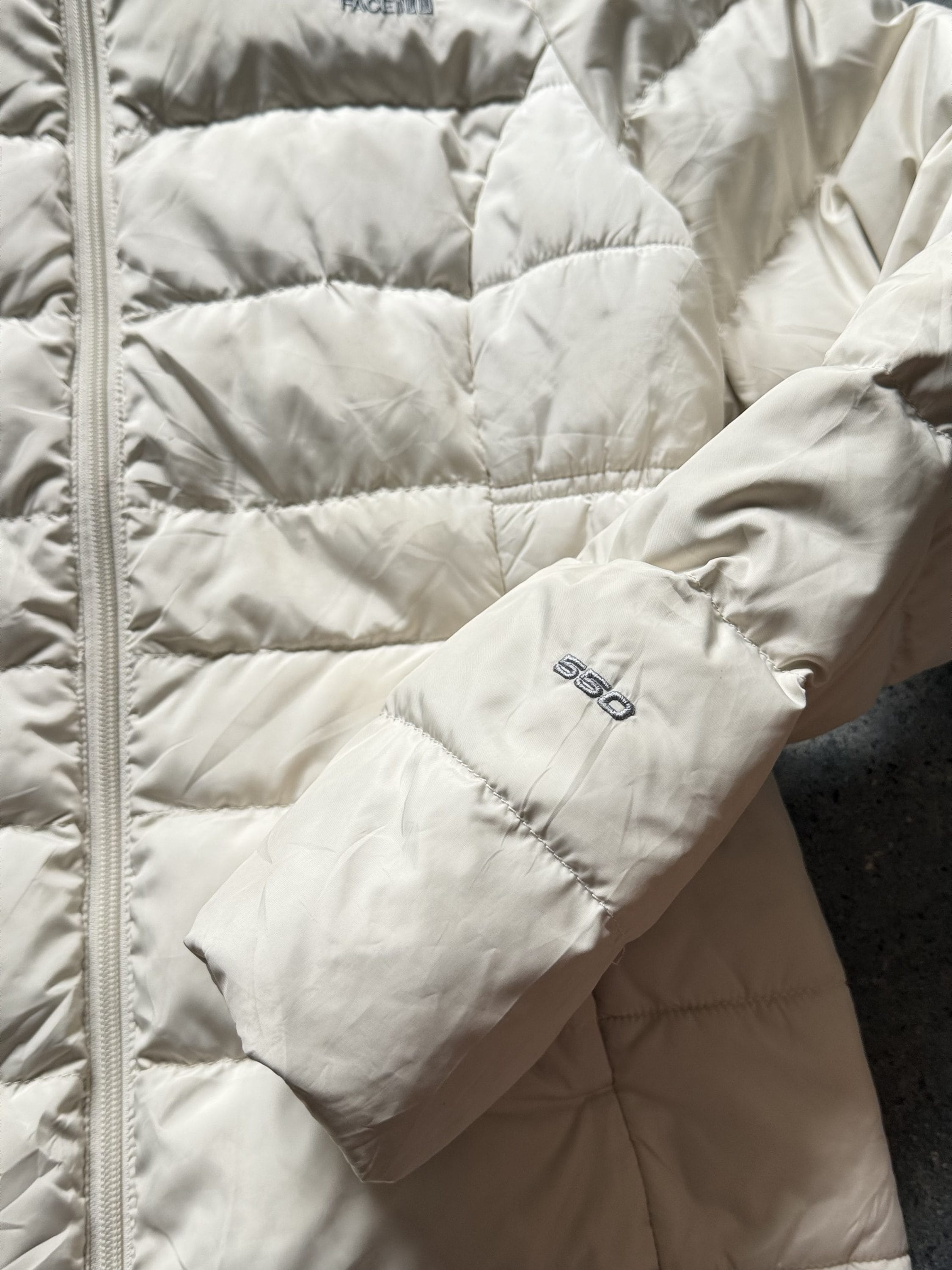 Close-up of a light-colored quilted puffer jacket with a front zipper and stitched panels.