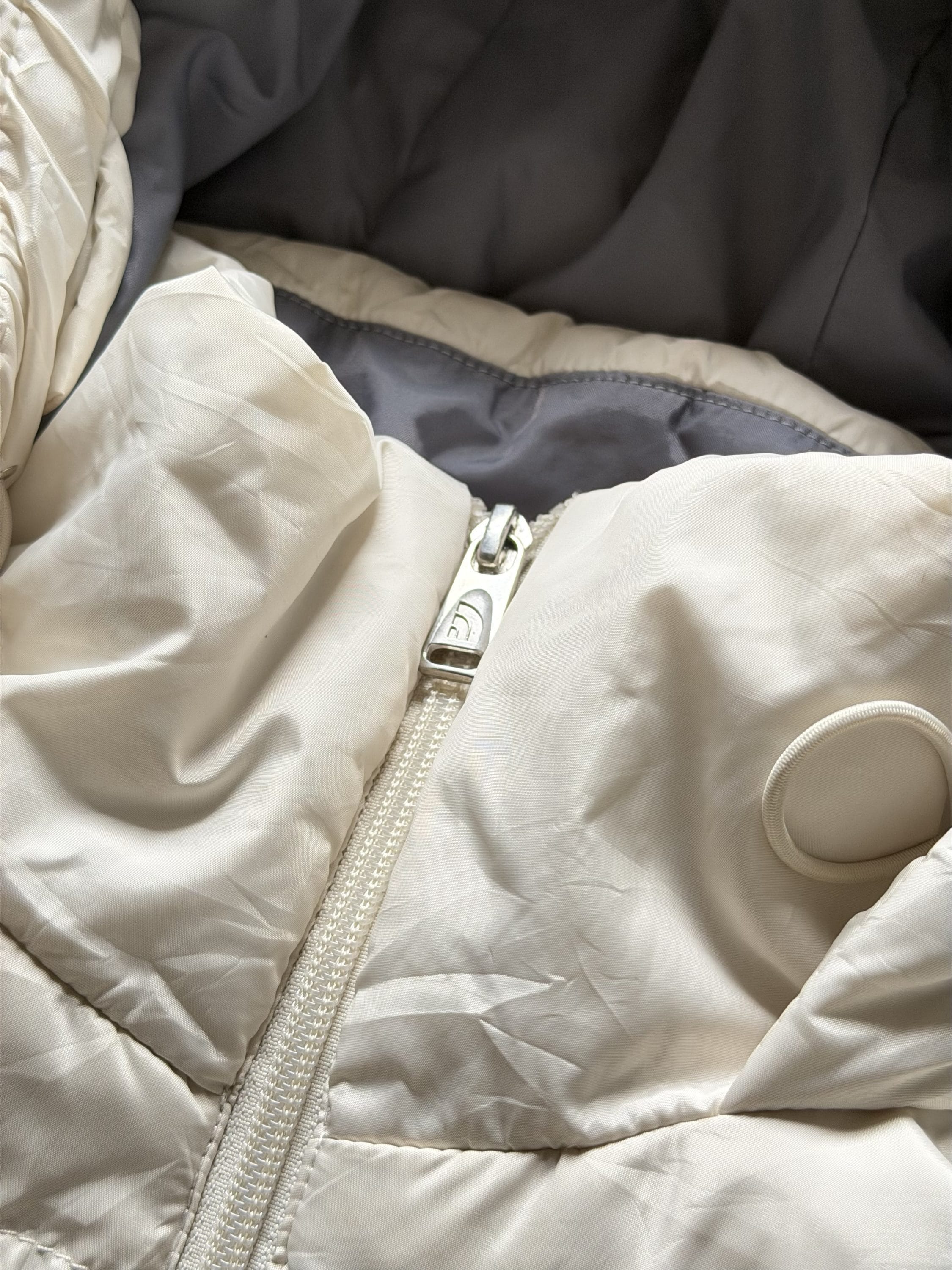 Close-up of a light beige padded jacket with a white zipper, partially open to reveal gray interior lining.