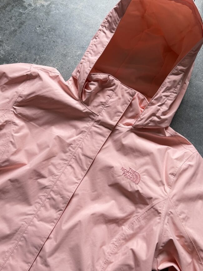 Light pink North Face rain jacket with hood laid flat, logo visible on chest area
