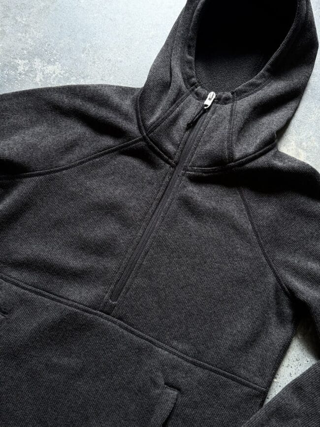 Close-up of a dark gray zip-up hoodie highlighting the zipper and textured fabric surface on a light background.