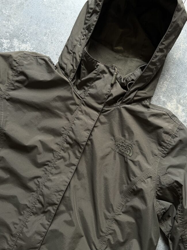 Close-up of a brown hooded jacket with zipper, The North Face logo visible on the chest area