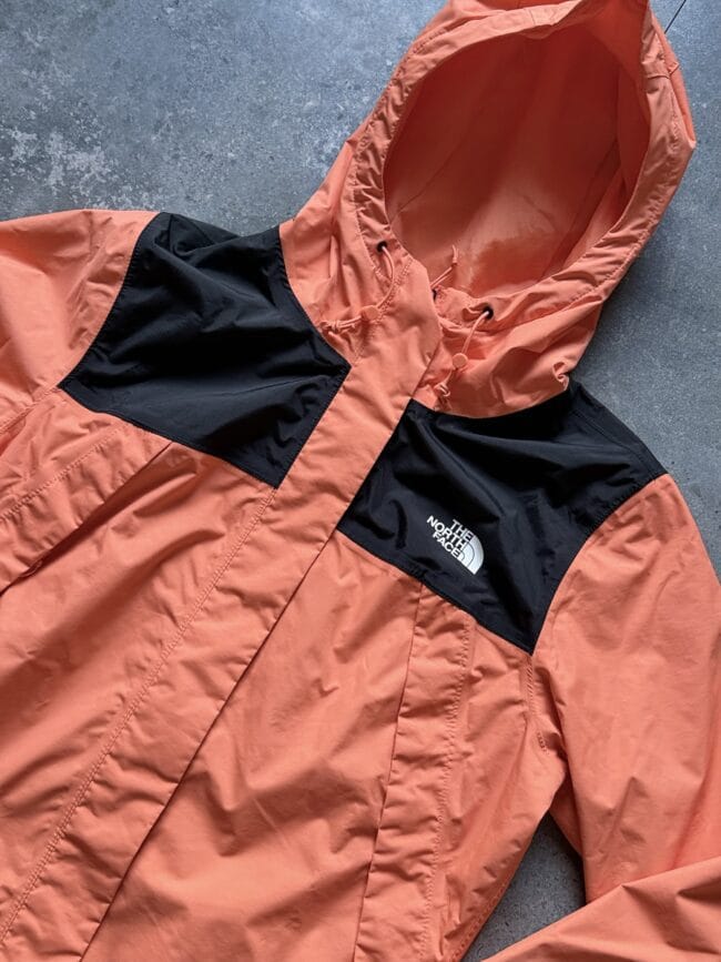 Orange lightweight jacket with a black chest panel and hood, The North Face logo on the left chest area.