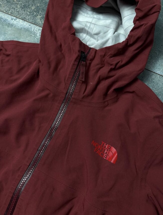 Maroon The North Face jacket laid flat, showing the front zipper and red logo on the chest.