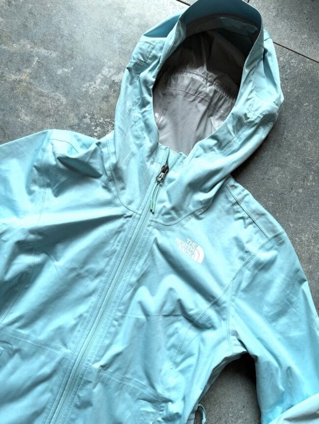 Light blue The North Face jacket laid flat with zipper closed and hood up, showing brand logo on chest.