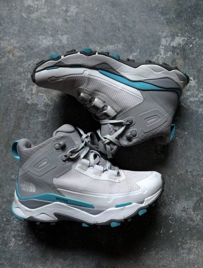 Pair of gray The North Face hiking boots with teal accents on a textured dark surface.