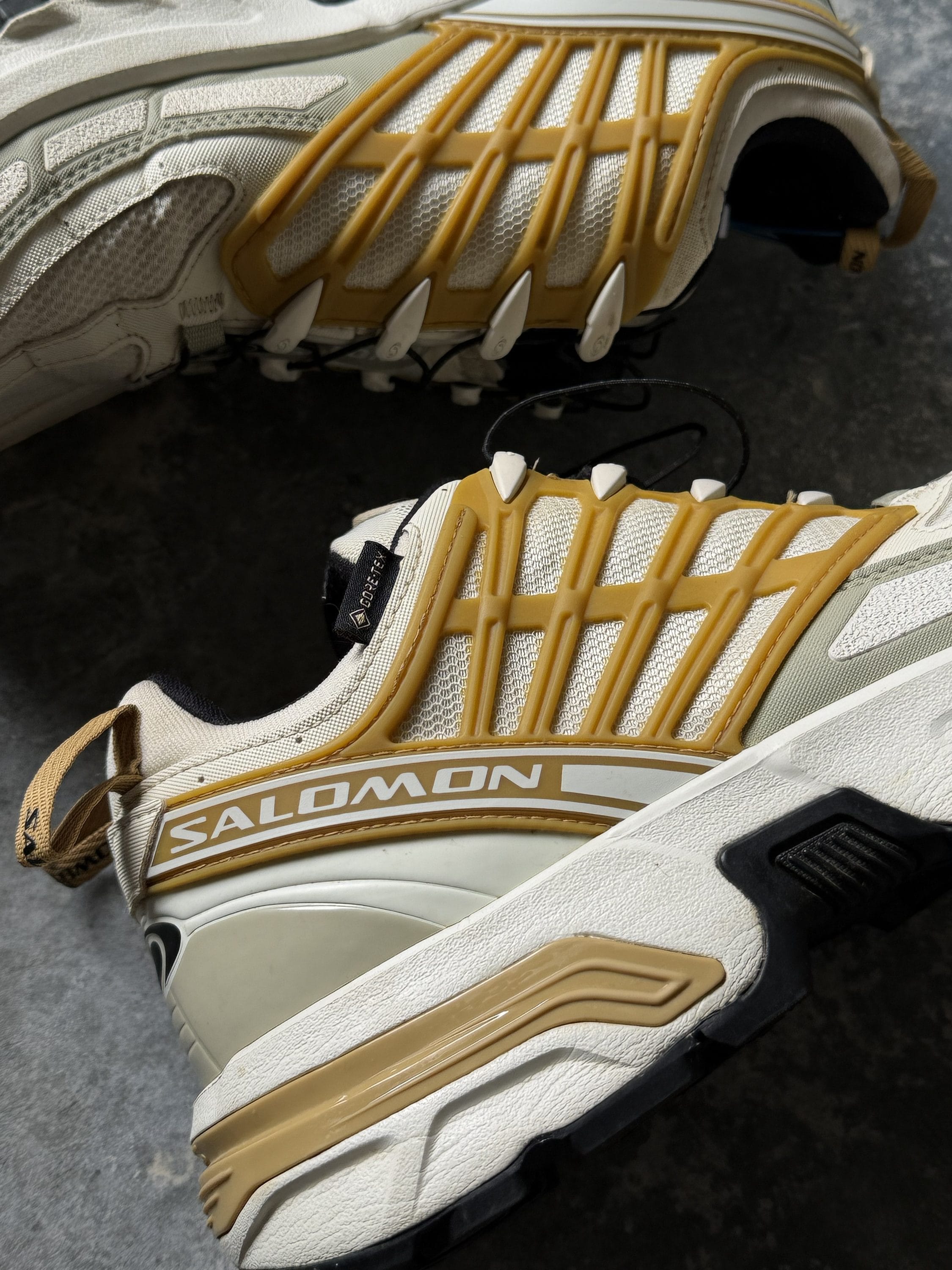 Pair of Salomon trail running shoes in white and tan with a distinctive segmented cage on the midfoot area for support.