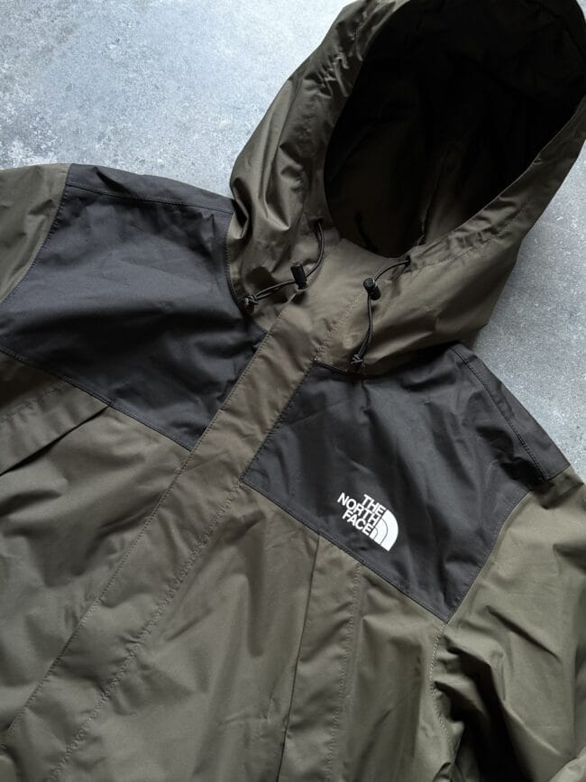 Olive and black The North Face hooded jacket laid flat, logo on the chest to the right of center.