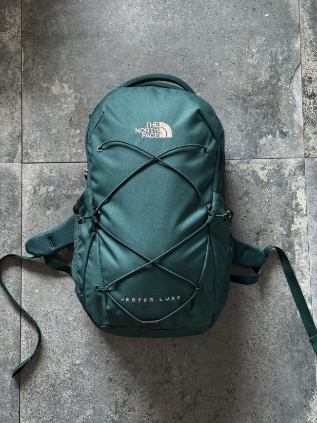 Teal The North Face backpack on a textured gray concrete floor, front bungee cords visible.
