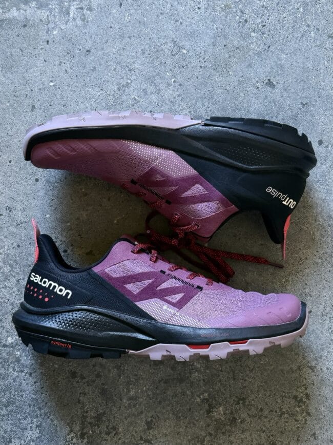 Pink and black Salomon trail running shoe photographed on a concrete surface, highlighting its design and grip outsole.