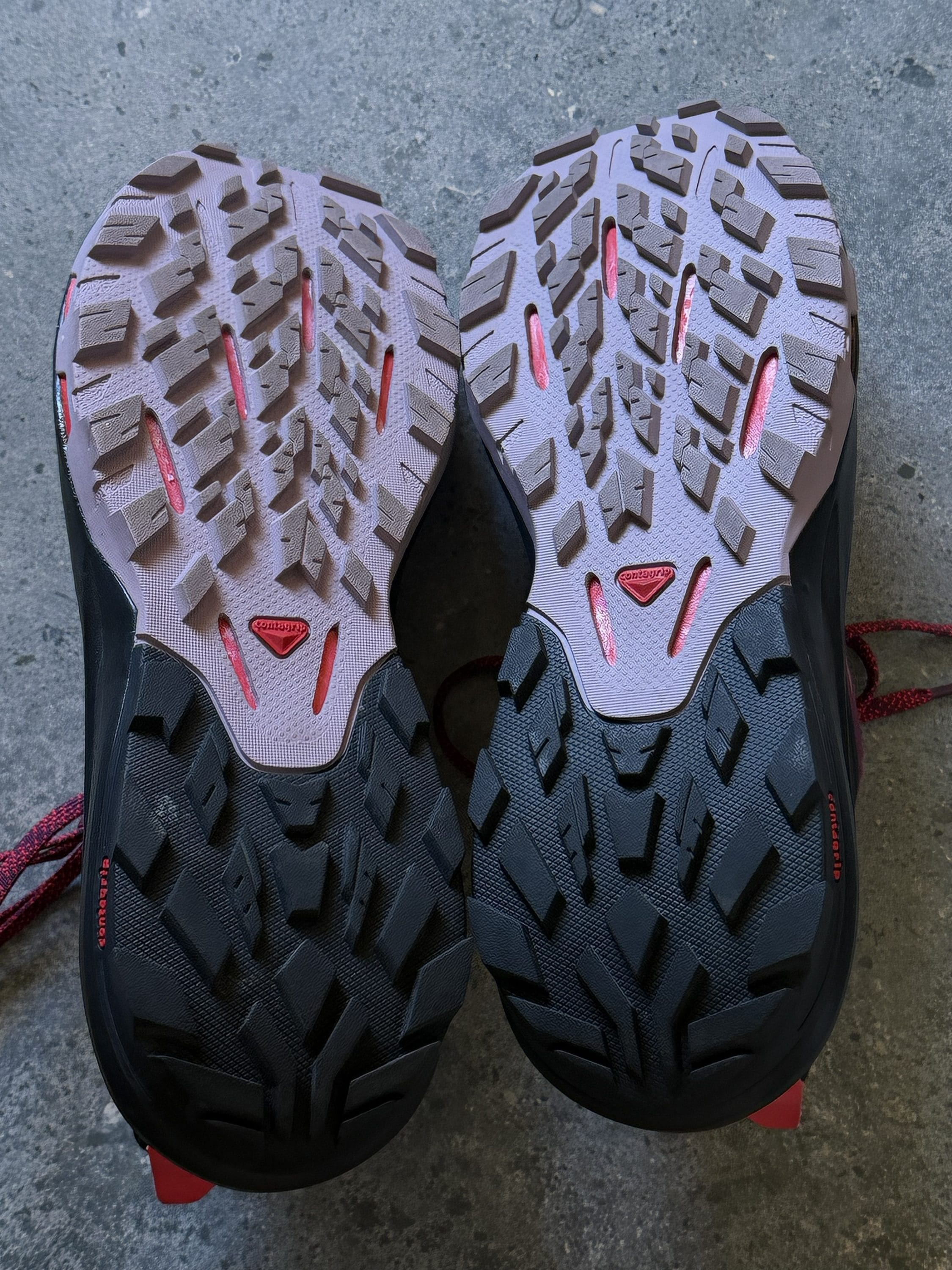 Top-down view of two trail running shoes with rugged, lugged outsoles and pink accents at the midsole.