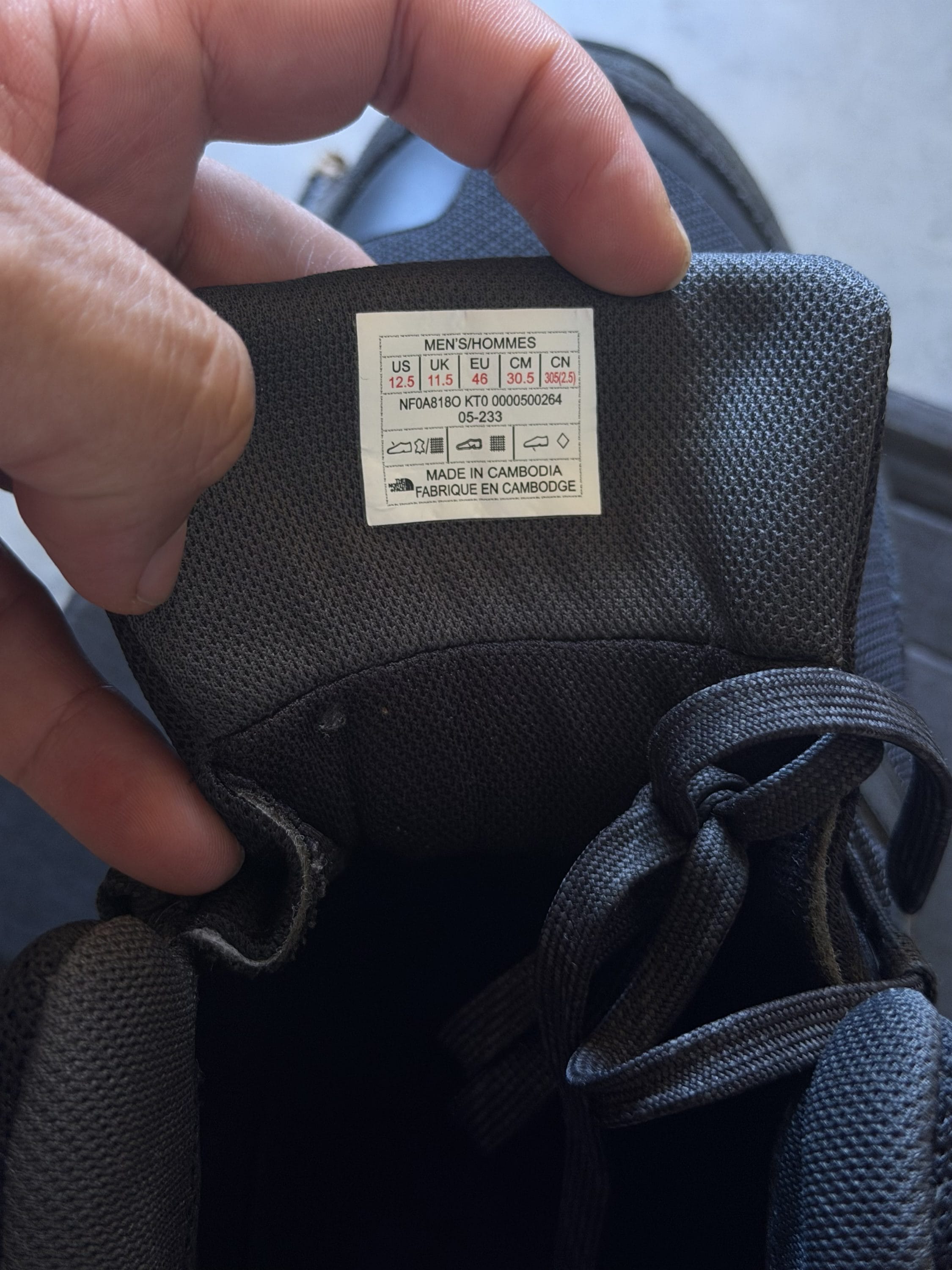 Label inside a dark athletic shoe showing men's US size 12.5, UK 11.5, EU 46, made in Cambodia, with care icons and product code.