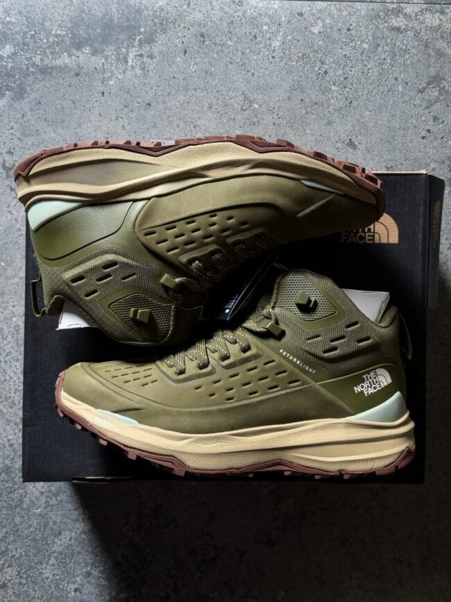 Olive green hiking boots with perforated panels and chunky brown soles resting on a black shoe box.